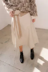 Pollera midi de eco cuero color beige, de corte recto y tiro alto, con costuras verticales decorativas y detalle de cinturón fino con flecos.