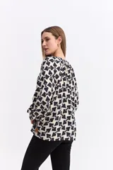 Blusa de corte relajado con estampado geométrico en tonos beige y negro. Presenta cuello en V con detalle de frunces, mangas largas abullonadas con puños elásticos y una caída fluida.