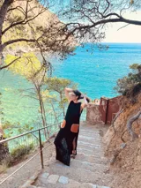 Vestido largo tejido de algodón color negro, sin mangas, con cuello redondo y tajos laterales. Presenta dos bolsillos de cuero color marrón en el frente.