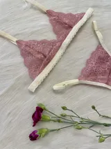 Conjunto de lencería compuesto por un corpiño triangular de encaje y una bombacha tipo tanga a juego. Ambas piezas presentan encaje en tono rosado con detalles de terminaciones en color crema.