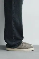 Zapatilla deportiva de hombre confeccionada en piel con acabado de serraje. Presenta un diseño minimalista con cordones al tono y un detalle en contraste de color en la pieza del talón. Cuenta con una suela de goma con volumen.