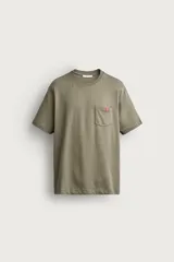 Camiseta verde militar de corte regular, con cuello redondo, manga corta y un bolsillo de parche en el pecho con etiqueta decorativa contrastante.