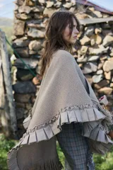 Ruana artesanal de lana merino en tono beige, con detalles de volados en lino en el borde y terminación con flecos largos.