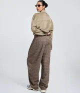 Pantalón de vestir de corte barrel, tiro alto con pliegues delanteros y pierna ancha, confeccionado en tejido con estampado de cuadros en tonos marrones y rojizos.