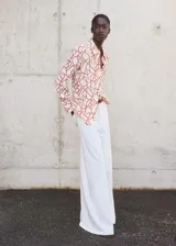 Camisa de corte recto con estampado abstracto en tonos rojizos sobre fondo claro. Presenta cuello camisero, cierre frontal con botones ocultos bajo tapeta y mangas largas con puños abotonados.