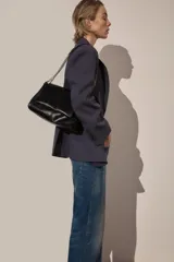 Bolso de hombro negro con detalle de costuras y tres compartimentos, uno con cierre de cremallera. Asa de hombro con cadena y cierre mediante imán.