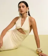 Vestido largo color crema, de tejido jersey, con escote halter y detalle de nudo/torcido en el busto que genera un recorte cutout central. El vestido es ajustado al cuerpo.