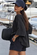 Remera oversize de algodón negro, con mangas cortas amplias, cuello redondo y un bolsillo aplicado en el pecho. Presenta un diseño holgado con dobladillo asimétrico más largo en la parte trasera y aberturas laterales.