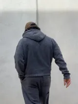 Conjunto de dos piezas compuesto por un buzo con capucha y cierre frontal y un pantalón de jogging, ambos confeccionados en tejido con efecto acid wash en color gris oscuro. El buzo cuenta con bolsillos frontales y logo bordado, mientras que el pantalón presenta un corte holgado y logo bordado en la pierna.