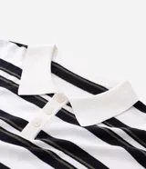 Remera boxy de punto listrado en blanco, negro y verde oliva, con cuello polo y abertura frontal con botones. Posee caída cómoda y textura suave.