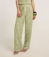 Pantalón sastre de corte recto y cintura alta, confeccionado en poliéster de color verde con bordados abstractos de líneas curvas en hilo de algodón. Presenta cierre tradicional y pliegues.