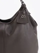 Bolso tipo hobo confeccionado en cuero vacuno negro con efecto rugoso y acabado suave. Presenta manijas finas para llevar al hombro, costura central vertical y un pequeño llavero de cuero colgante con el logo de la marca.