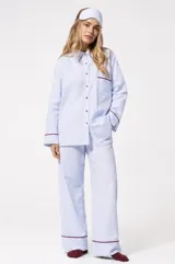 Pijama de dos piezas de algodón con estampado de rayas celestes y blancas. Incluye una camisa de manga larga con botones y ribetes en contraste, y un pantalón largo de corte recto y holgado con elástico en la cintura y ribetes en el ruedo.
