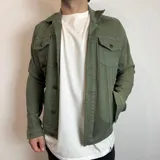 Chaqueta de jean color verde militar con cuello clásico, cierre frontal con botones metálicos, cuatro bolsillos frontales con solapa y puños abotonados.