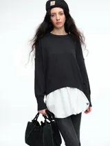 Sweater de punto color negro, con cuello redondo, hombros caídos y terminaciones acanaladas en puños y ruedo. Presenta un diseño de calce relajado y tejido suave.