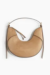 Cartera de mano de gamuza sintética color tostado, con diseño curvo en forma de U, cierre superior y tiras colgantes decorativas. Incluye asa corta superior y herrajes metálicos dorados.