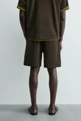 Bermuda de hombre color verde oscuro, de corte relajado y tiro medio. Confeccionada en tejido texturado, presenta cintura elástica con cordón de ajuste interno y bolsillos laterales y trasero de vivo.