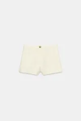 Short de tiro alto confeccionado en tweed negro, con cierre frontal y botón dorado decorativo.
