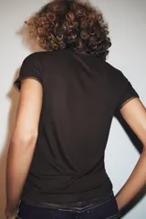 Camiseta de manga corta color marrón oscuro con textura acanalada, cuello redondo y bajo recto. Presenta un bajo superpuesto de tul o tela más clara, visible en el ruedo y en el cuello.