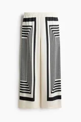 Pantalón de satén fluido color blanco y negro con estampado geométrico de líneas concéntricas, cintura elástica y piernas anchas.