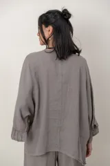 Blusa de lino color verde militar, holgada, de manga 3/4 con volados en los puños, cuello redondo y detalle de alforzas horizontales en el dobladillo.