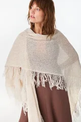 Ruana de punto color beige con diseño abierto y flecos en los bordes.