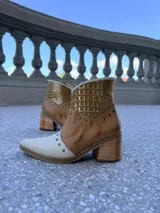 Bota tejana de cuero combinado en napa y croco, con puntera y caña en tonos beige y tostado, y detalle metalizado dorado. Presenta tachas decorativas en la puntera y el empeine, y cuenta con taco de madera de 6,5 cm.