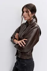 Cazadora de efecto piel en color marrón chocolate, con cuello clásico, cierre frontal con cremallera, bolsillos laterales y puños con botón.