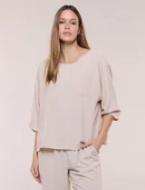 Blusa oversize de color beige con caída fluida, cuello redondo y bolsillo aplicado en el pecho. Cuenta con mangas tres cuartos de hombro caído y diseño liso.