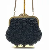 Bolso tipo sobre de estilo vintage, bordado íntegramente con mostacillas negras formando un patrón de ondas. Presenta una boquilla metálica dorada con cierre a presión y una cadena fina dorada para llevar al hombro.