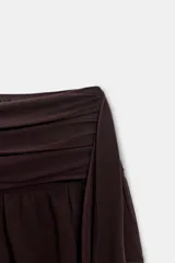 Falda pantalón de tiro medio en color bordó, con diseño de volantes y detalle asimétrico lateral. Cuenta con cierre lateral mediante cremallera oculta.