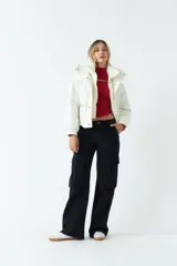 Campera puffer cropped color blanco, de corte a la cintura, con cuello alto, cierre metálico frontal con botones a presión y bolsillos laterales con cierre invisible.