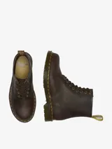 Borcego Dr. Martens 1460 de 8 ojales, color marrón oscuro, confeccionado en cuero Crazy Horse con aspecto desgastado. Presenta cordones marrones, ojales dorados, tirador de talón amarillo y costura amarilla distintiva en la suela con cámara de aire.