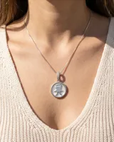 Dije circular de plata 925 con centro de nácar y silueta de niño en relieve. El pasante está decorado con circonias brillantes y se presenta con una cadena de plata fina.