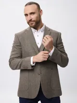 Blazer de tweed en tonos marrones con diseño de espiga, presenta coderas en contraste, cierre frontal con botones y bolsillos laterales de parche.