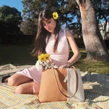 Cartera tipo tote de cuero sintético con diseño combinado en tono gris y blanco, textura granulada, asas largas para el hombro y cierre superior.