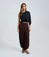 Pantalón de corte aladino confeccionado en viscosa y poliéster, con diseño de rayas verticales y acabado con leve transparencia. Presenta cintura alta, trabillas para cinturón y puños elásticos en el dobladillo.