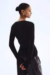 Top negro de manga larga en tejido de punto acanalado fino. Presenta un escote en V profundo con una pequeña abertura frontal cerrada con dos corchetes ocultos.
