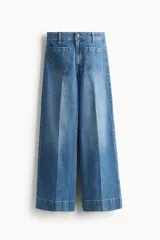 Jean de denim de algodón con leve stretch, tiro alto y pierna ancha de corte holgado. Cuenta con bolsillos de parche delanteros y traseros, y cierre de botón y cremallera.