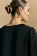 Blusa negra de satén con escote en V y detalle de volados frontales. Presenta mangas largas con puños abotonados y una silueta fluida.