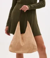 Cartera tipo hobo de gran tamaño confeccionada en material sintético efecto gamuza color tostado. Presenta una estructura flexible, asa única en tono contrastante y cierre mediante botón a presión.