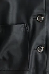 Campera corta negra de efecto cuero, con cuello camisero, cierre frontal de botones y dos bolsillos parche grandes en el frente.