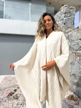 Ruana tejida en color crudo con diseño de trenzas y textura en relieve. Presenta un corte amplio y envolvente, ideal para usar como capa sobre otras prendas.