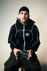 Campera hoodie negra con cierre frontal, bolsillos tipo canguro, capucha con cordón ajustable y detalles de ribete blanco. Presenta un logo con un globo terráqueo y el número 27 en el pecho y un estampado de una estrella con incrustaciones en la espalda.