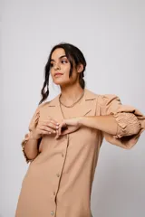 Vestido corto color tostado, con cuello solapa, abotonado al frente y mangas 3/4 con puños fruncidos.