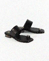 Sandalia plana de cuero color negro, con una tira ancha superior con textura, tira separadora de dedo con detalle metálico y suela con tachas doradas decorativas.