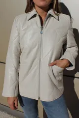 Campera de cuero color beige con diseño acolchado en forma de rombos, cuello camisero, cierre frontal metálico y bolsillos laterales.
