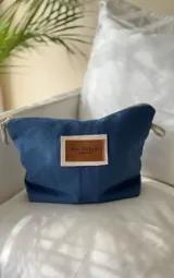 Nécessaire de lona azul con cierre superior y parche de cuero sintético marrón con el logo de la marca en el frente.
