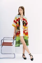 Kimono largo de lino con estampado vibrante que simula un paisaje de atardecer con palmeras, en franjas horizontales de colores cálidos y verdes. Posee mangas amplias y lazo para ajustar en la cintura.