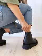 Botas negras de cuero con caña baja, cierre lateral con cremallera y suela track.